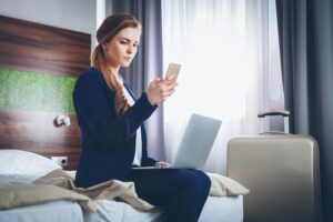 Hotel Trends 2023 - kobieta w pokoju hotelowym pracująca przy laptopie, wybierająca telefoniczny kontakt